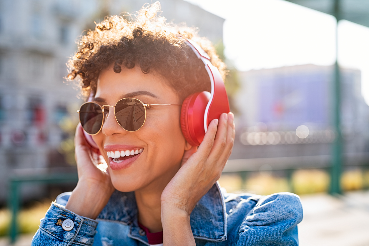 Young adult smiling while they wear sunglasses and red headphones.