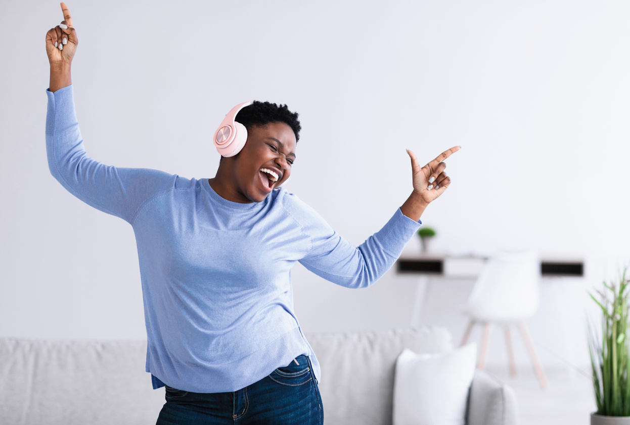 African american woman in a light blue shirt dancing while wearing white headphones.