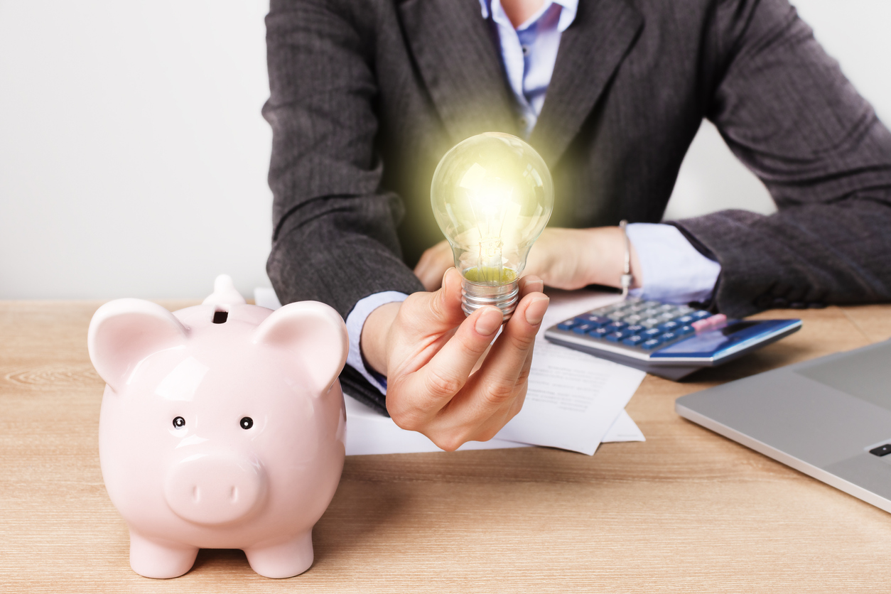 person holding lightbulb with a piggy bank on a desk