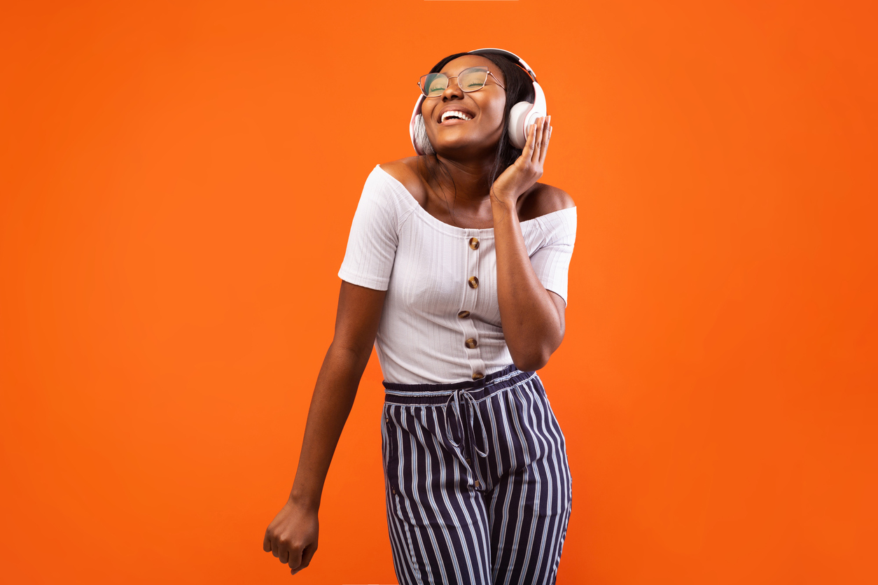 Girl in white headphones smiling in front of an orange background.