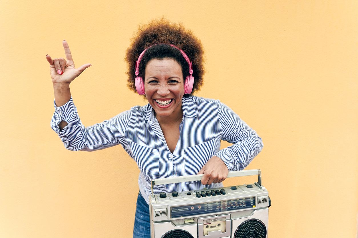 Woman wearing pink headphones and holding a boombox.