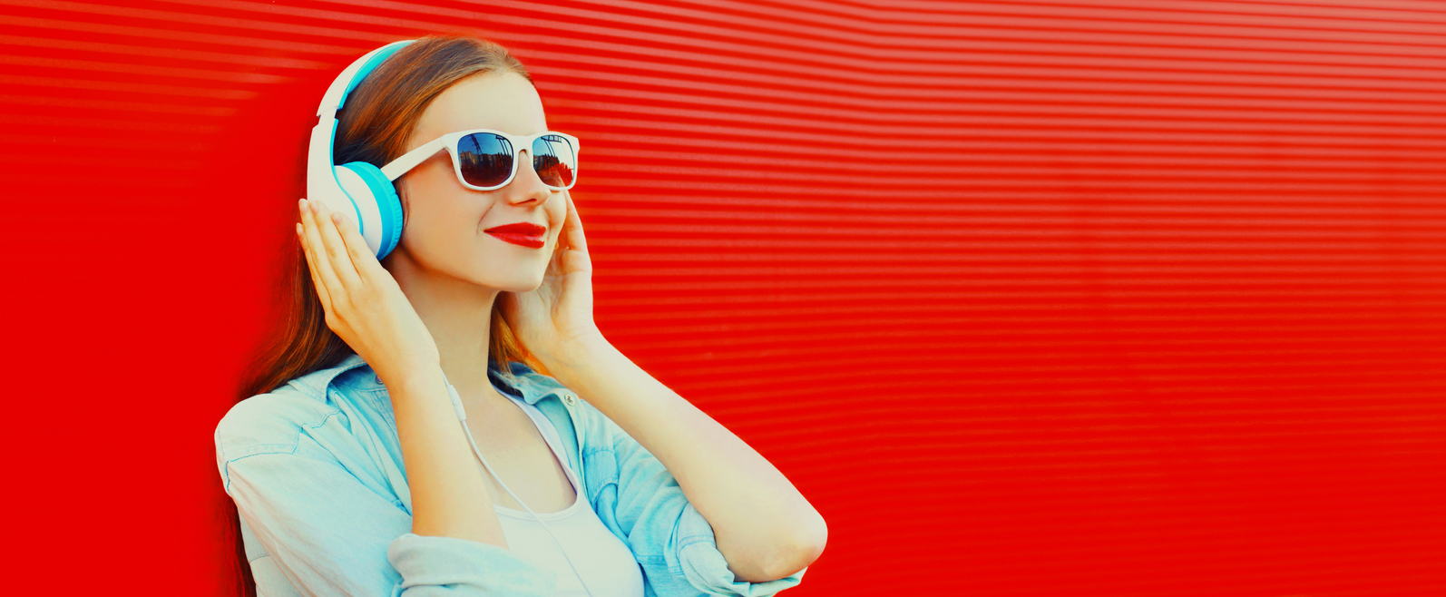 Woman in a blue shirt with headphones on a red background.